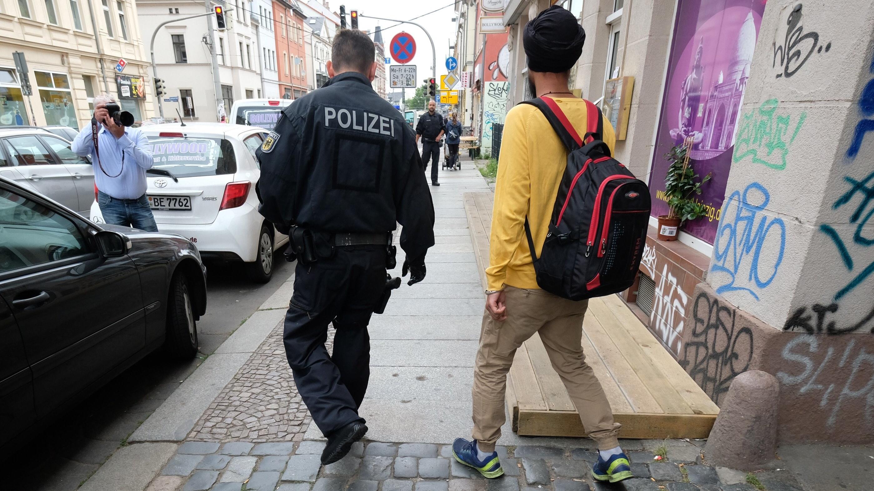 Scheinehen-Razzia in fünf Bundesländern: Hunderte Polizisten im Einsatz gegen Schleuser 13.06.2018, Sachsen, Leipzig: Ein Beamter der Bundespolizei begleitet einen Mann aus einem Mehrfamilienhaus im Leipziger Stadtteil Plagwitz. Dort findet ein Polizeieinsatz im Zusammenhang mit Scheinehen statt. Foto: Sebastian Willnow/dpa-Zentralbild/