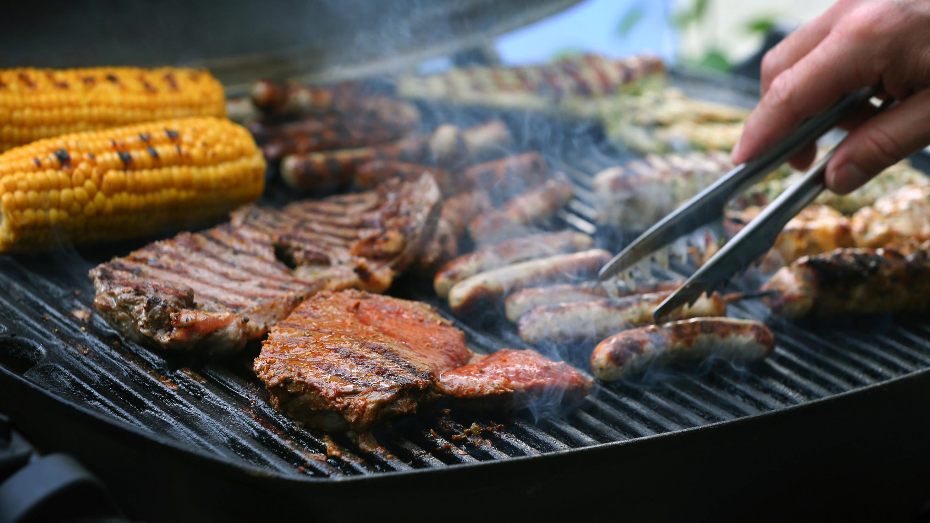 Gasgrill: Vermeiden Sie diese Fehler beim Grillen mit Gas Maiskolben, Fleischspieße, Bratwürste und Steaks liegen auf dem Rost eines Gasgrills.